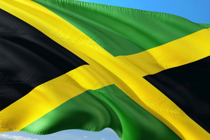 Flag of Jamaica waving in the wind against deep blue sky. High quality fabric.